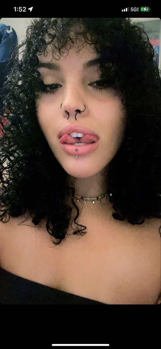 a close up of a person with curly hair and piercings on her nose wearing a choker