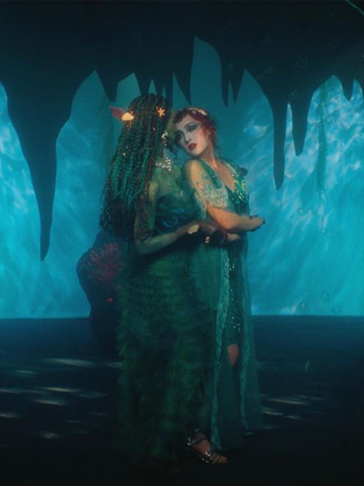 a woman in a green dress standing next to a giant blue cave with ice formations on the walls