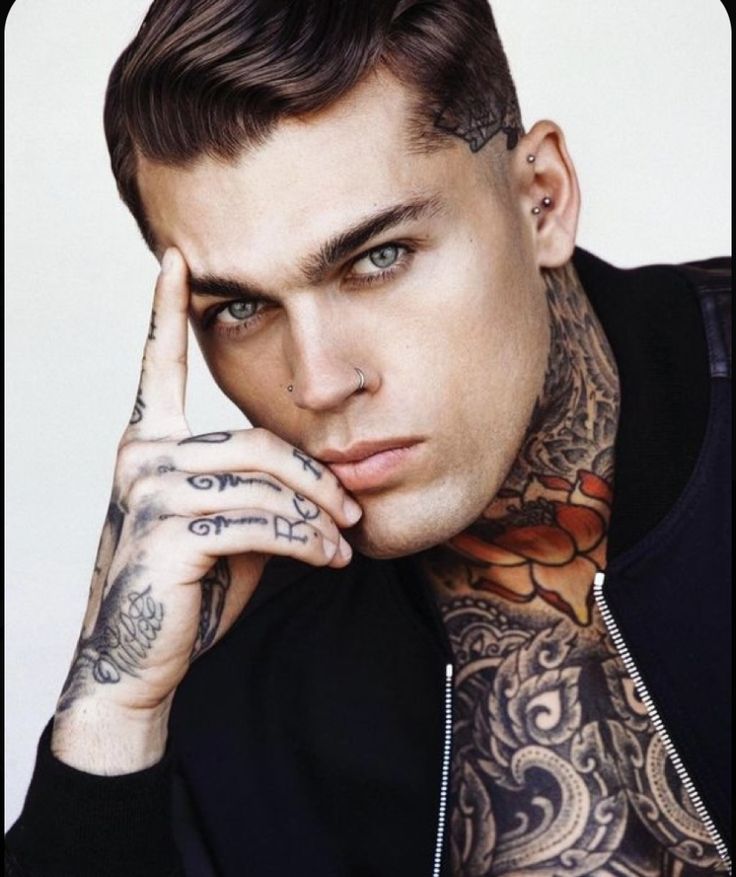 a man with tattoos and piercings on his arm posing for a photo in front of a white background