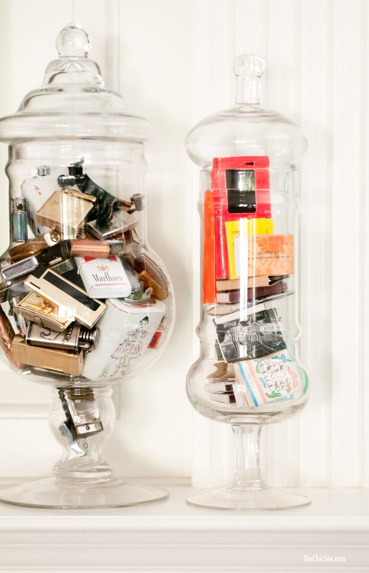 two glass jars filled with various items on top of a white shelf next to each other