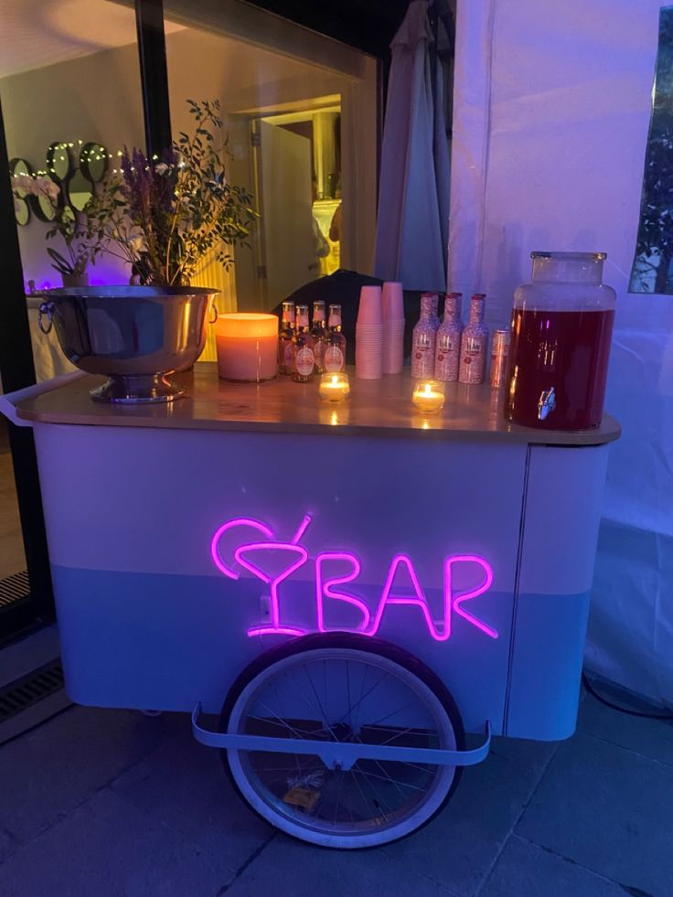 a bar cart with candles and bottles on the counter in front of a building at night