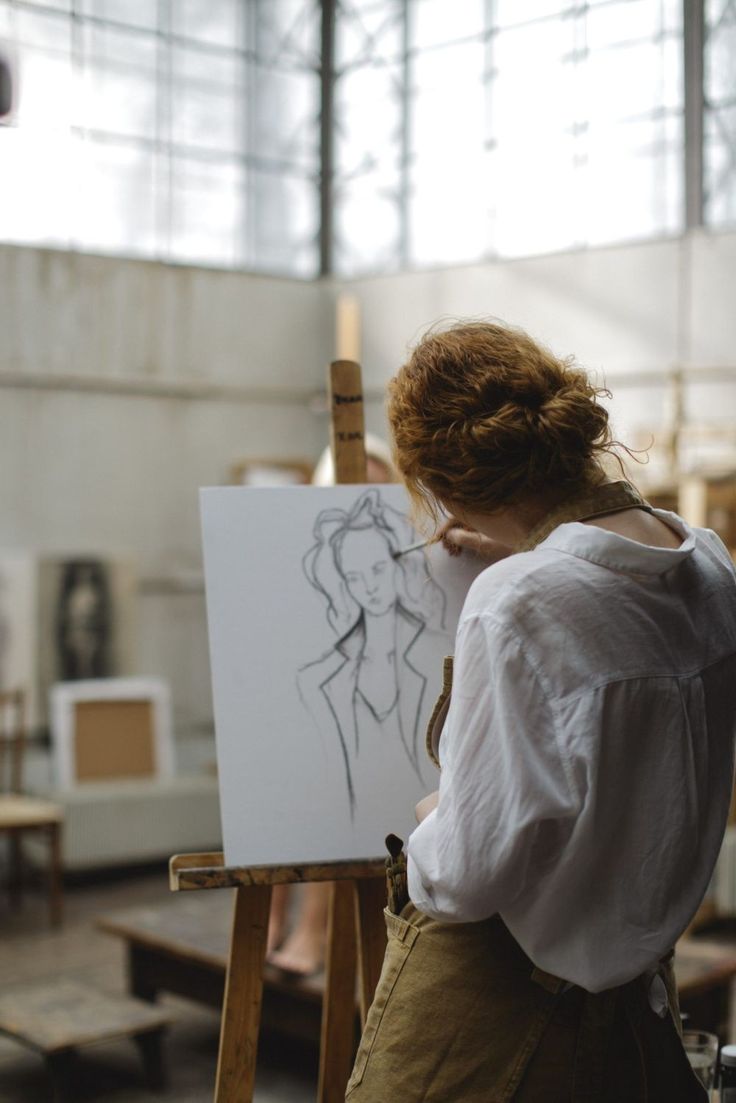 a woman standing in front of an easel with a drawing on it's side