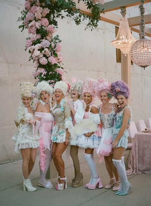 a group of women standing next to each other in front of a pink flower covered building