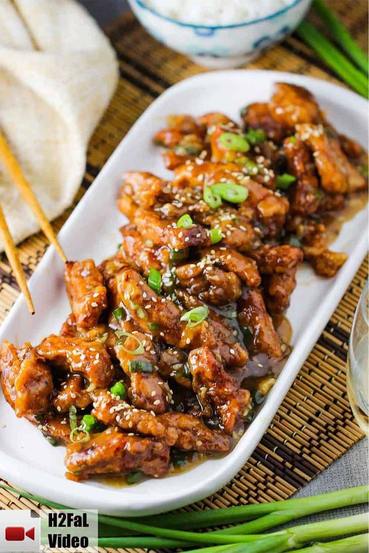 chicken with sesame seeds and green onions served on a white platter next to chopsticks