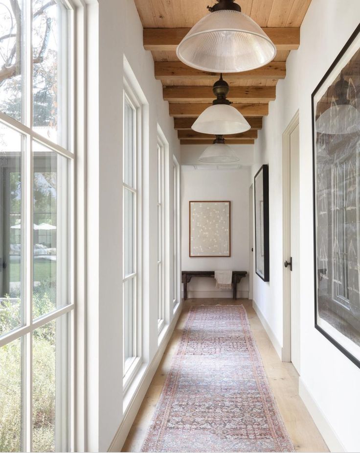 a long hallway with white walls and wood ceilinging is flanked by two large windows