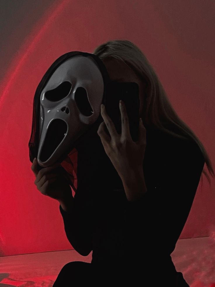 a woman holding a mask up to her face in front of a red light background