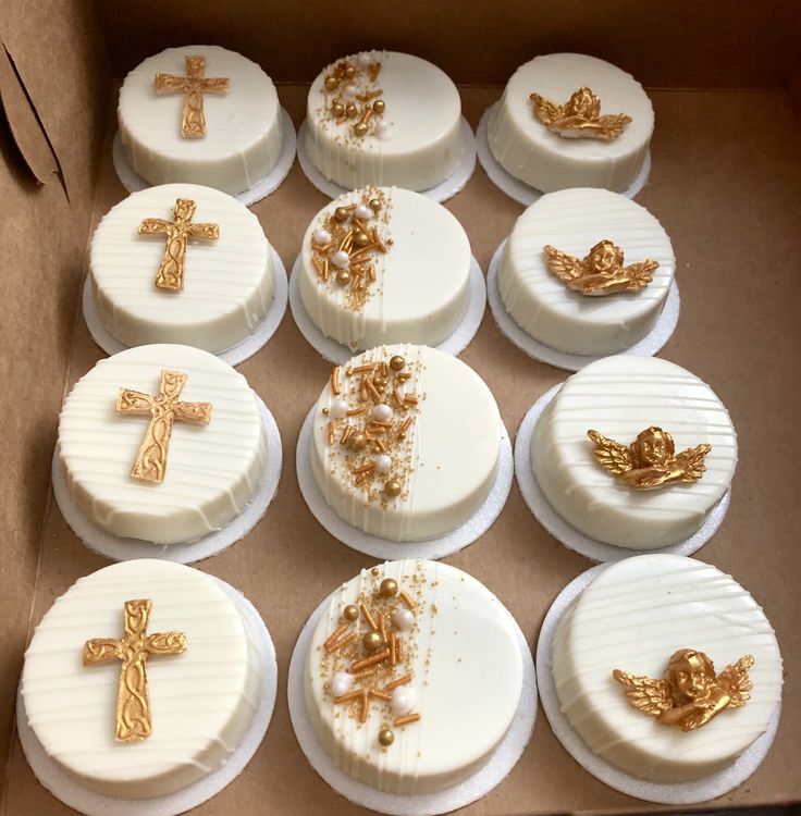 a box filled with lots of white cakes covered in gold crosses and angel decorations on top of each cake