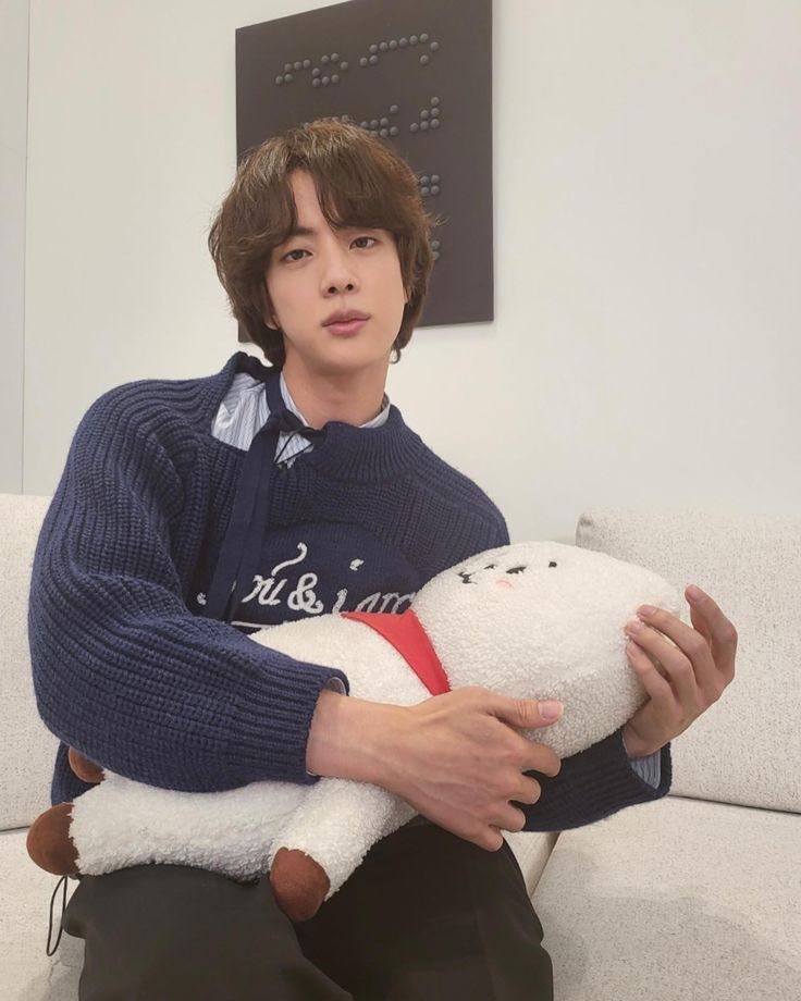 a person sitting on a couch with a stuffed animal in his lap and wearing a sweater