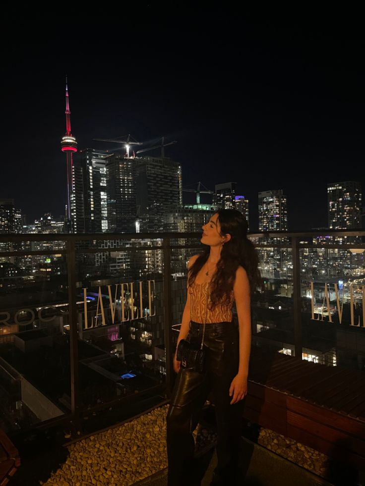 a woman standing on top of a roof in front of a city skyline at night