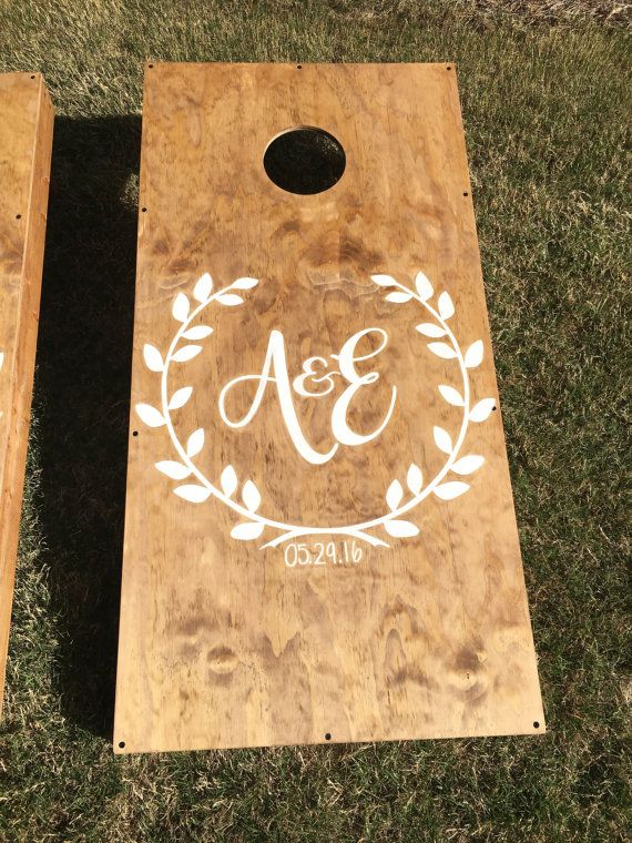 two personalized cornhole game boards on the grass with initials and laurel wreaths