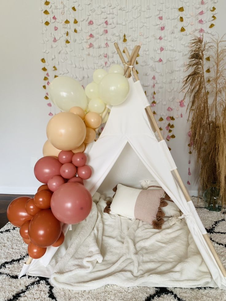 a teepee tent with balloons in front of it and a rug on the floor