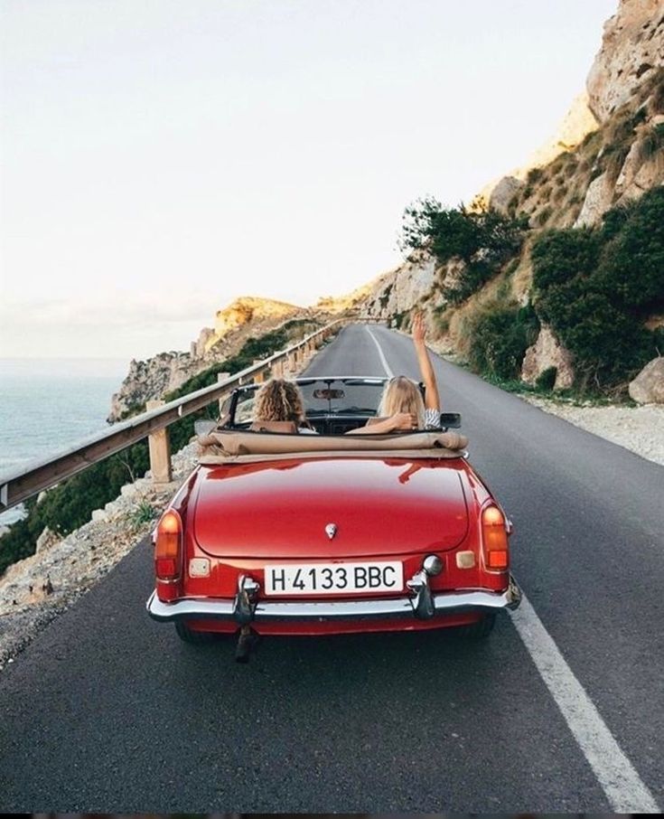 a red convertible car driving down a road next to the ocean