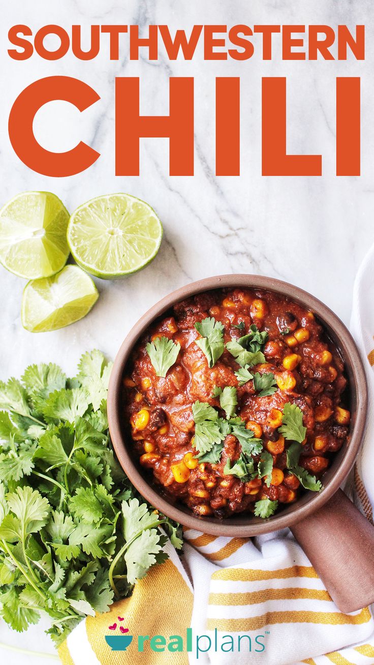 a bowl filled with chili next to cilantro and limes on a table