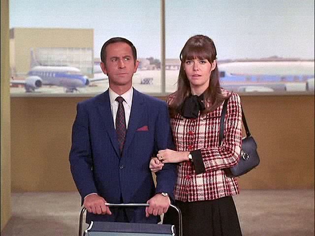 a man and woman standing next to each other in an airport holding a luggage cart