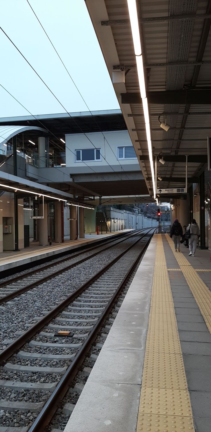 a train station with people walking on the platform and one person waiting for the train