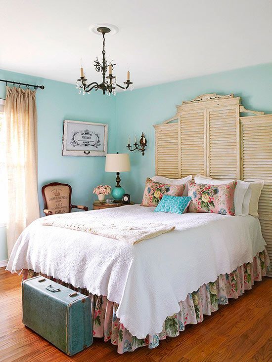 a bed sitting in a bedroom under a chandelier next to a window with shutters