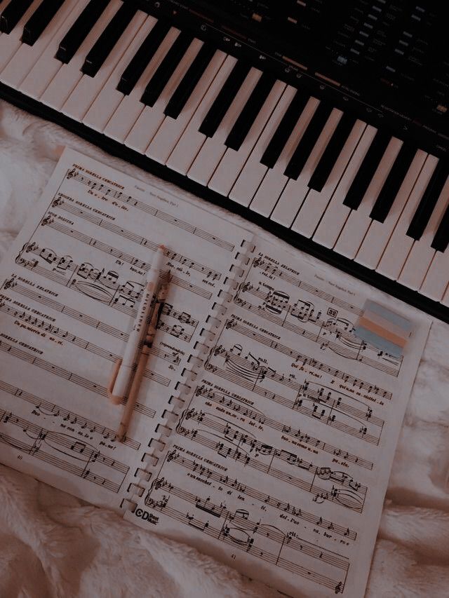 sheet music and pen laying next to piano keyboard