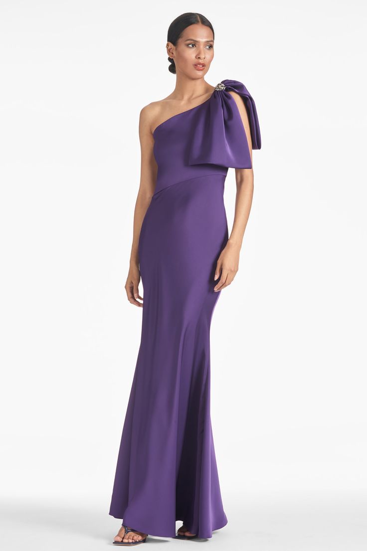 a woman in a long purple dress with one shoulder and bow at the top,