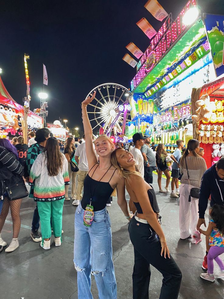 two women standing next to each other in front of an amusement park ride area at night