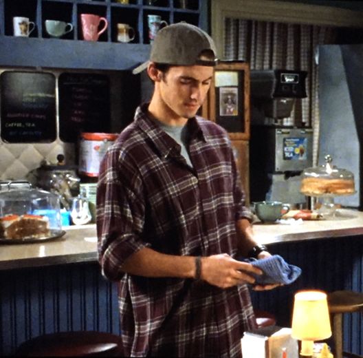 a young man standing in front of a counter holding a blue glove and looking at his cell phone