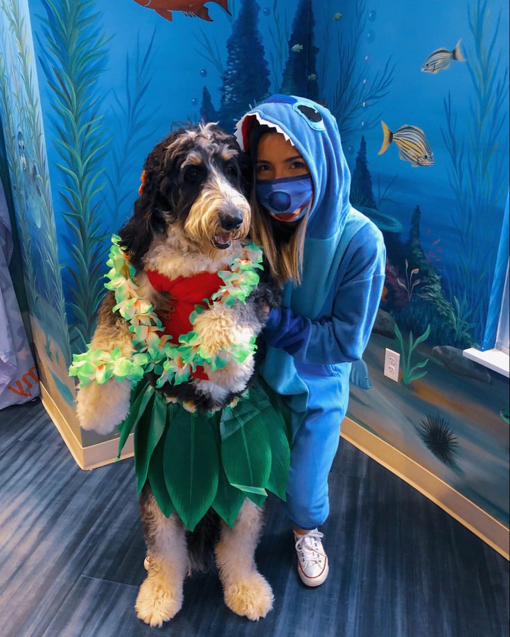 a woman is hugging her dog while wearing a green outfit and mask in front of a fish tank