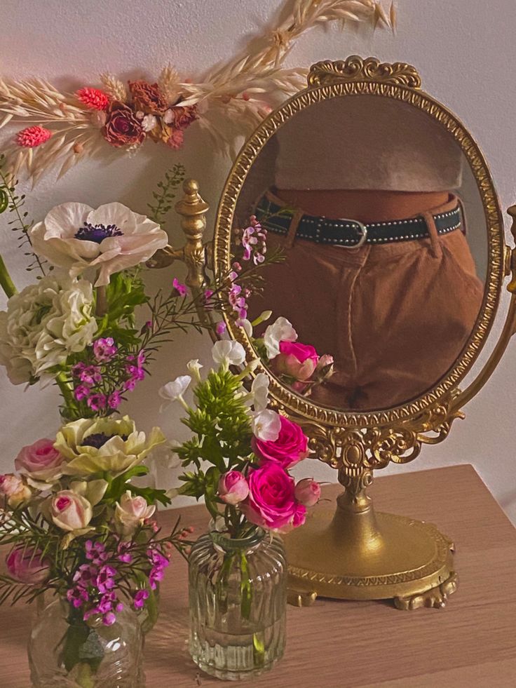 there is a vase with flowers in it and a mirror on the table next to it