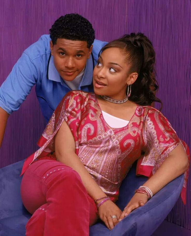 a man and woman sitting on top of a blue chair next to each other in front of a purple wall