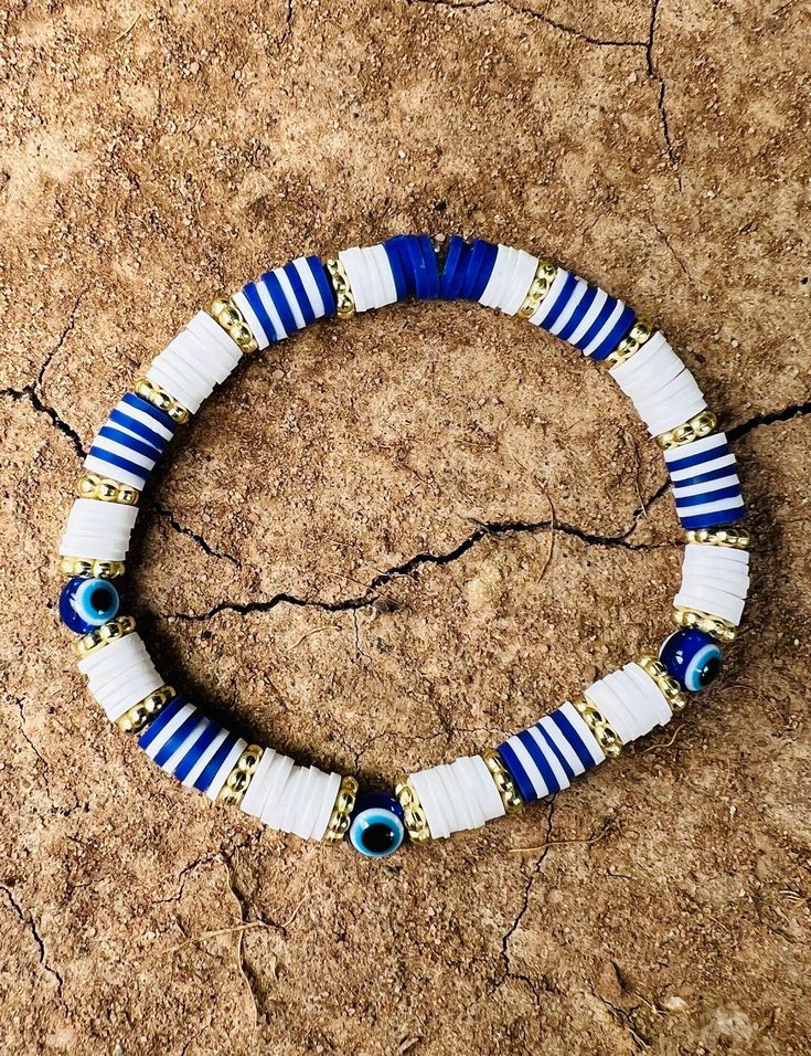 a blue and white beaded bracelet with evil eyes on the inside is sitting on a rock