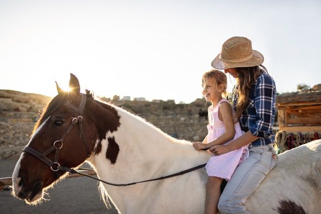 two children riding on the back of a brown and white horse