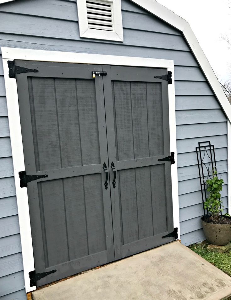 a gray garage with two doors and a planter in the yard next to it