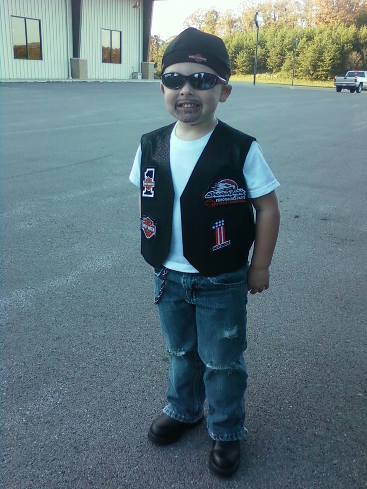 a young boy wearing sunglasses and a vest standing in the middle of an empty parking lot