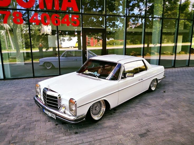 an old white car is parked in front of a building with glass doors and windows