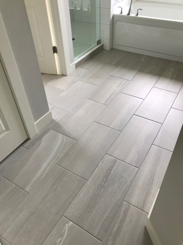 a bathroom with gray tile floors and white tub