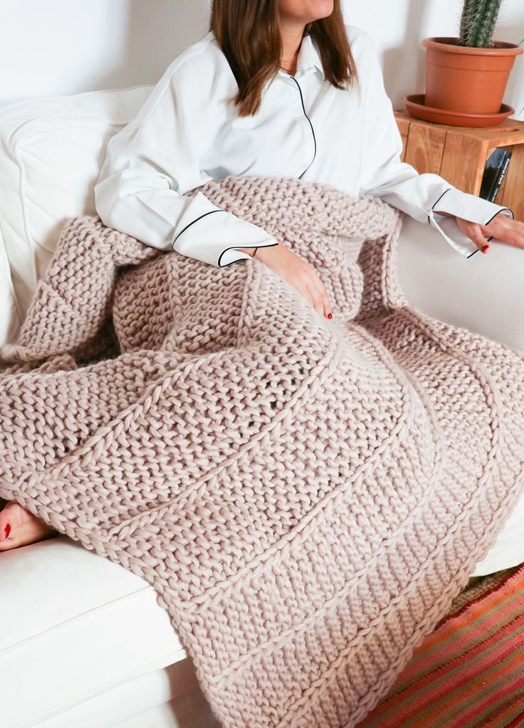 a woman is sitting on a couch with a knitted blanket in front of her