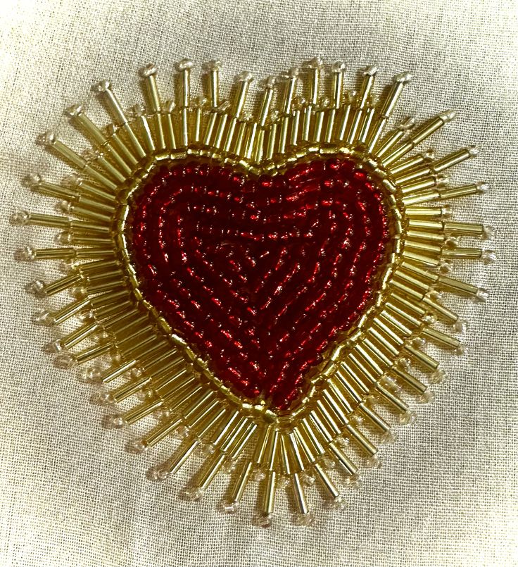 a red and gold heart brooch sitting on top of a white cloth