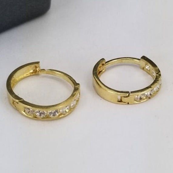 Beautiful hoop earrings in 14k gold with synthetic zirconia stones. All for only $85 Hoop measures 2mm width, 9mm circumference, and a clip-on closure. Purchase includes a gift box. Gold Channel Set Huggie Jewelry, Gold Cubic Zirconia Huggie Earrings Round Cut, Gold Round Cut Huggie Earrings, Dainty Huggie Hoop Earrings For Formal Occasions, Gold Hoop Huggie Earrings With Channel Set, Gold Huggie Hoop Earrings With Channel Set, Classic Gold Huggie Earrings Channel Set, Classic Gold Channel Set Huggie Earrings, Yellow Gold Cubic Zirconia Channel Set Huggie Earrings