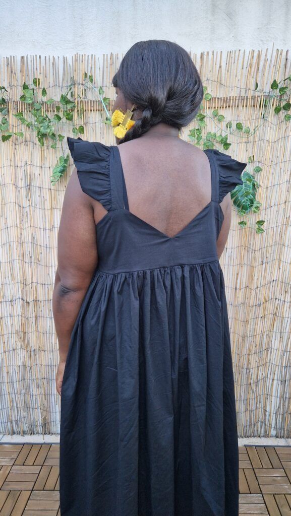 a woman standing in front of a bamboo fence wearing a black dress with ruffled sleeves