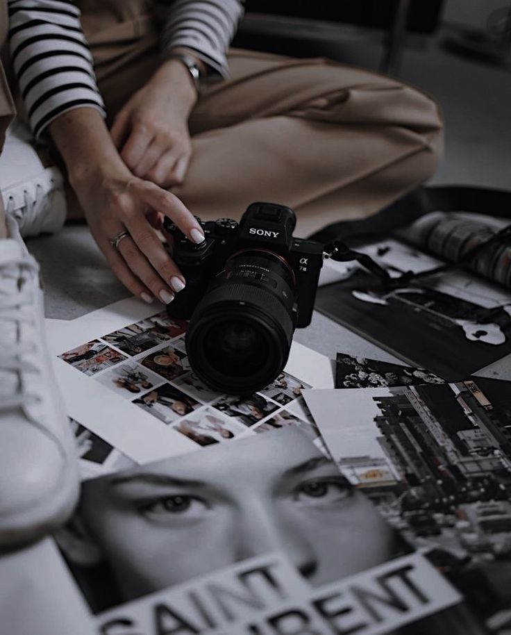 a woman sitting on the floor with a camera in front of her and several photographs surrounding her