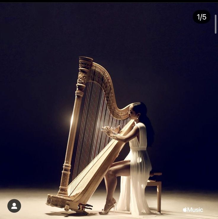 a woman sitting on a stool holding a harp in front of her face and looking down at the strings