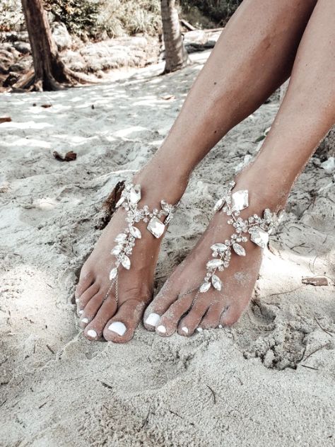 a barefoot woman's feet in white sand with flowers on the toes and toenails