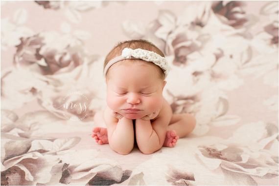 a baby is laying down on a blanket with her hands under her chin and looking at the camera