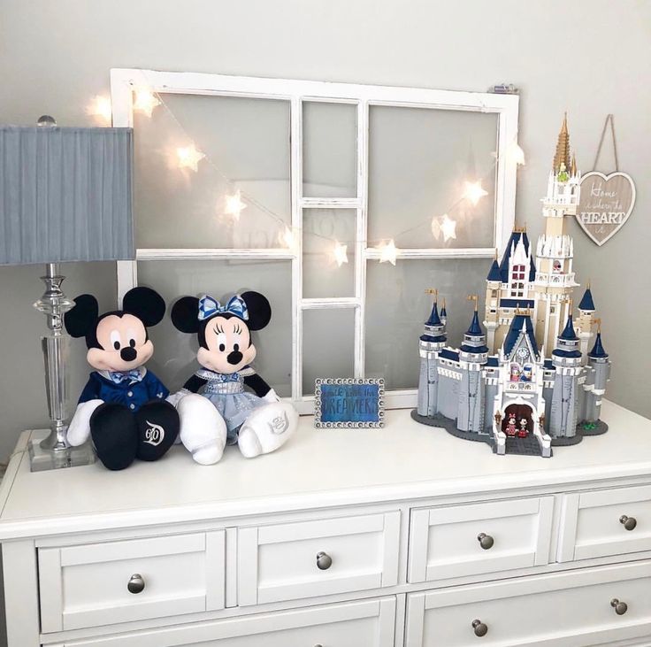 two stuffed animals sitting on top of a white dresser next to a window and castle