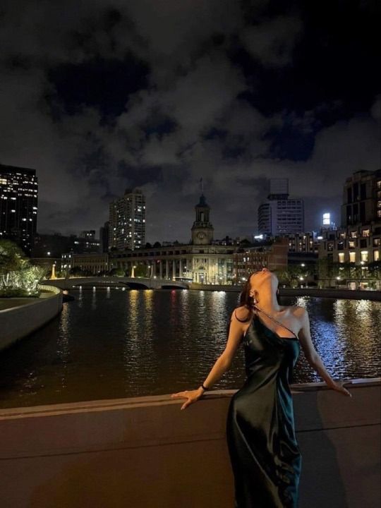 a woman in a long black dress standing on a ledge next to the water at night