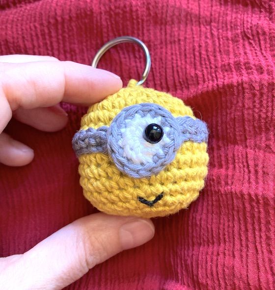 a hand holding a yellow and gray crocheted keychain with a minion on it