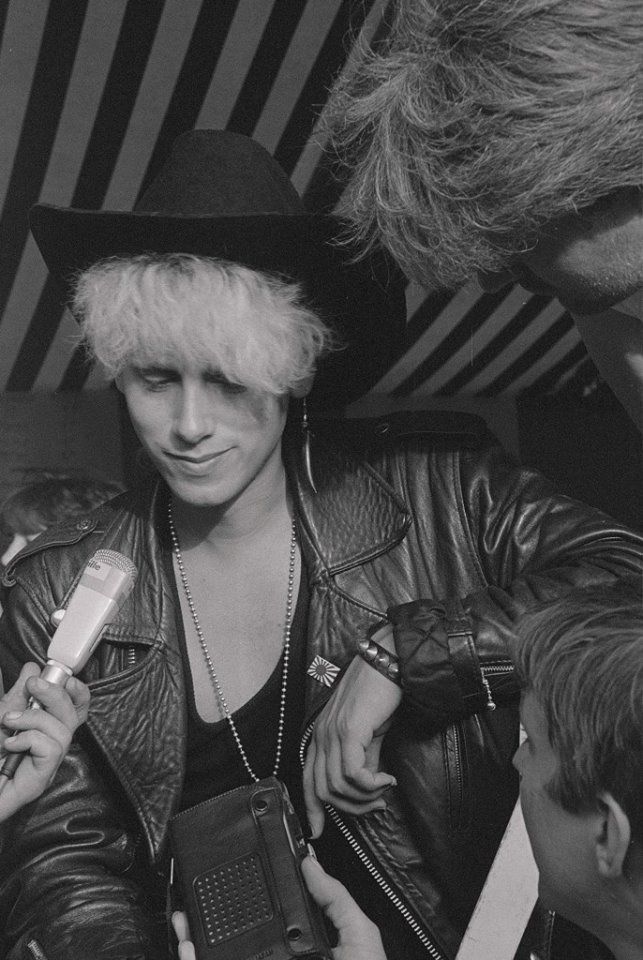 black and white photograph of woman in leather jacket holding electronic device with man looking on