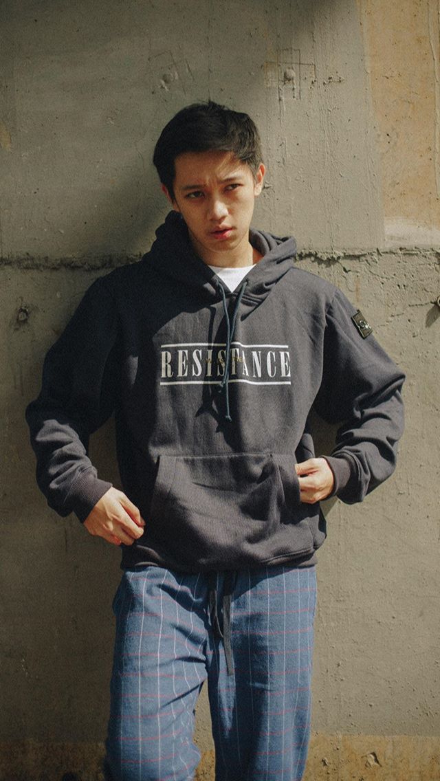 a young man standing in front of a wall wearing a hoodie and sweatpants