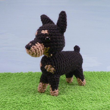 a crocheted black and brown dog standing on top of green carpet next to water