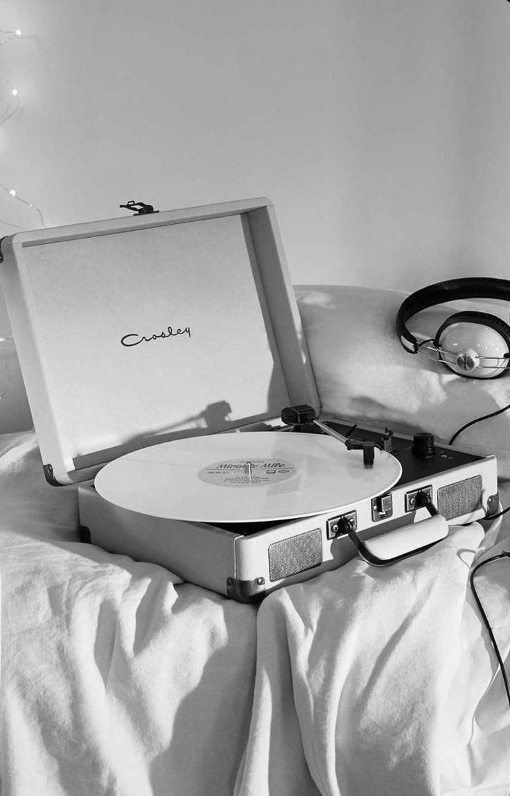 a record player sitting on top of a bed next to headphones and an mp3 player