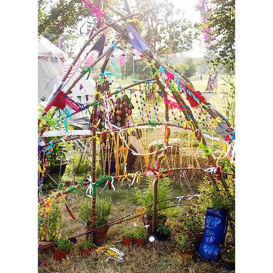 a tent that has been decorated with ribbons and streamers in the grass, surrounded by potted plants