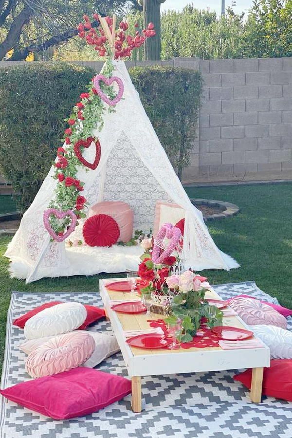 a teepee tent is set up in the yard with pillows and flowers on it